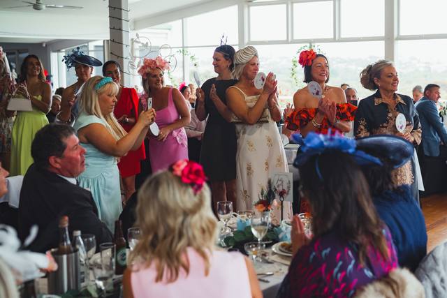 Guests in hats and fascinators applauding at the 2025 event